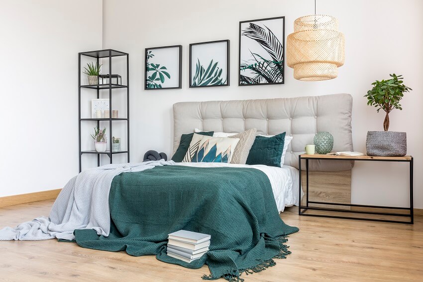 Plant on table next to bed with green bedding blanket and grey bedhead in bedroom interior