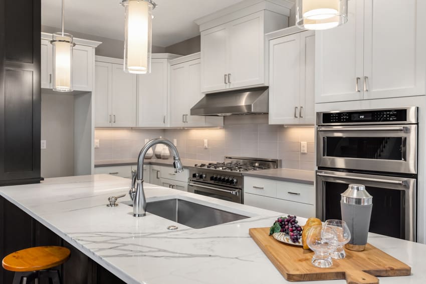 Subway backsplash and countertop in kitchen sink faucet oven hood white cabinets hanging lights