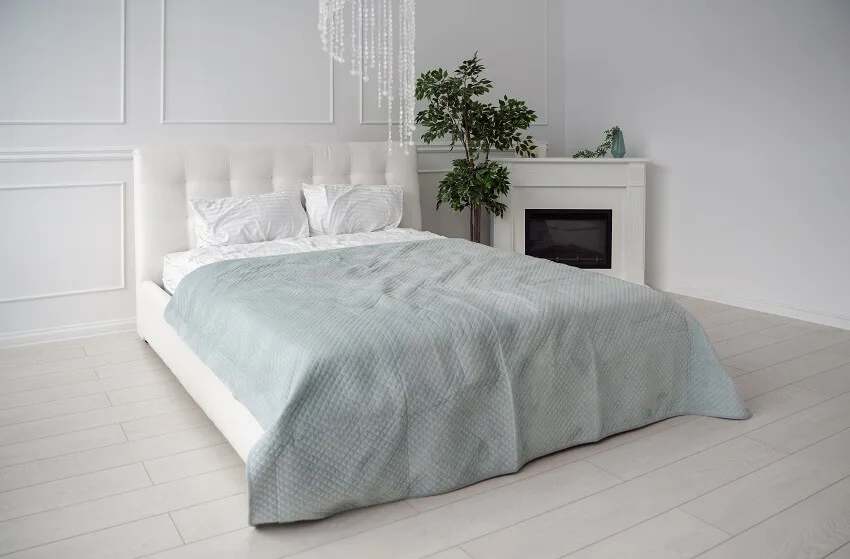 Side view of white leather bed with blue bedsheet and fireplace