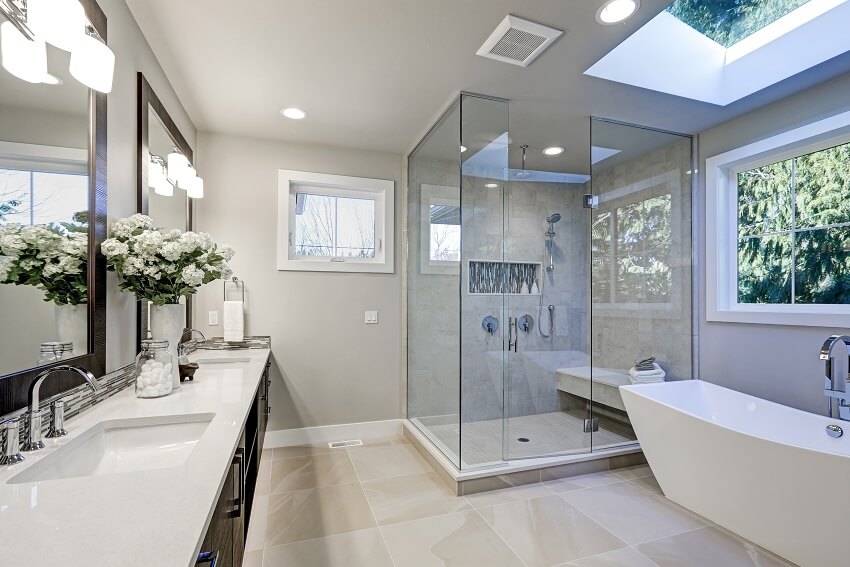 Spacious bathroom in gray tones with heated floors, freestanding tub, walk in shower, double sink vanity and skylights