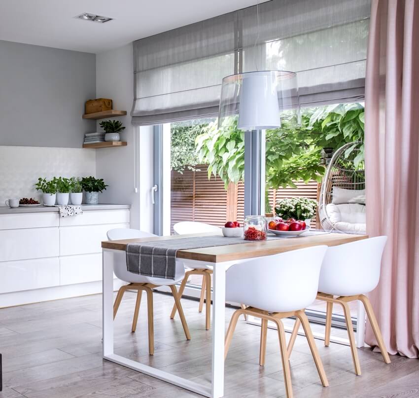 Spacious dining room interior with white chairs by a wooden table and sliding doors with roman shades 