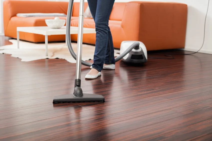 Woman cleaning the floor with vacuum and orange couch