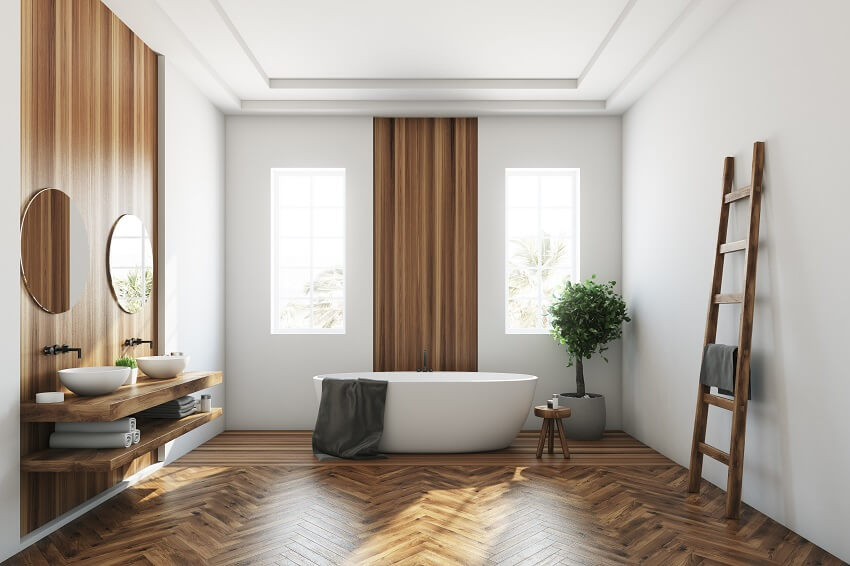 White and wooden bathroom with a vinyl wallpaper, wooden floor, a white tub and two narrow windows 