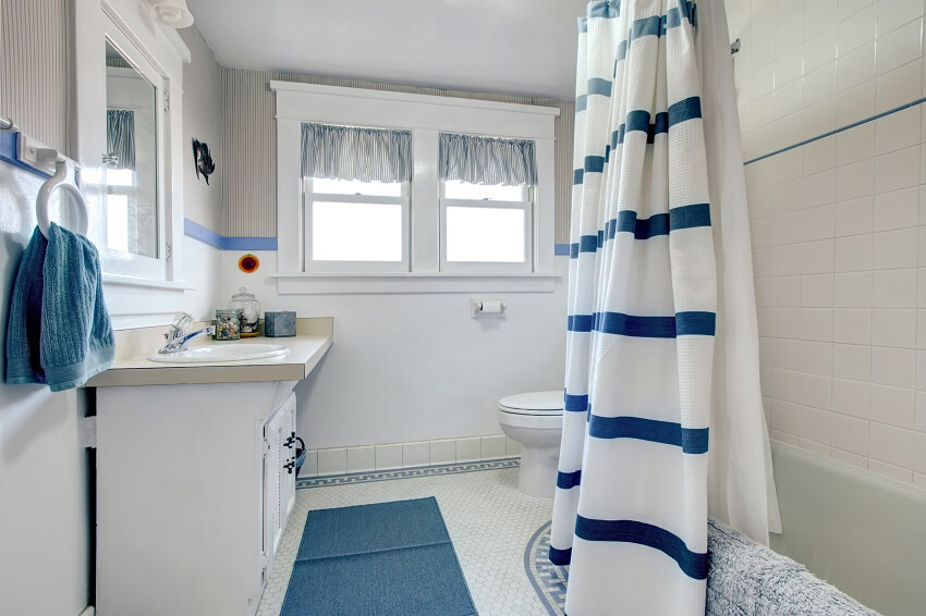 White bathroom with white washbasin cabinet blue rug and striped curtains