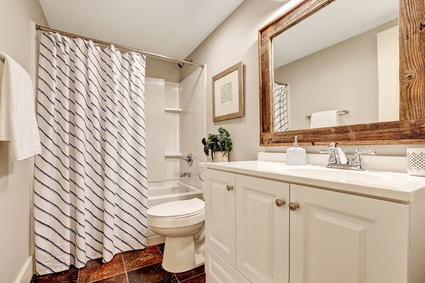 White tones bathroom with vanity cabinet and wooden framed mirror decorated with picture plant pot and striped curtain