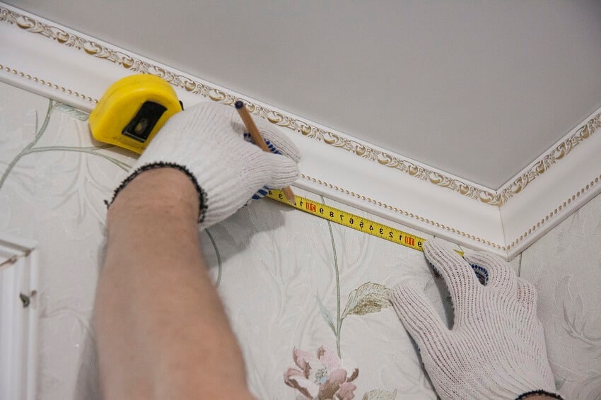 Worker in gloves preparing for installation marking for curtain rod with pencil and tape measure under ceiling