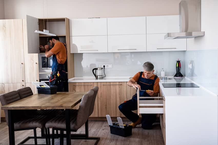 Workers in uniform repairing and assembling kitchen cupboard cabinet using screwdriver indoors