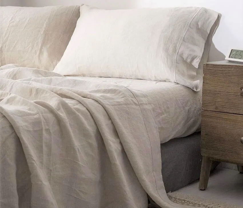 A bed with simple and opulence washed king size linen sheet and a bedside wooden table