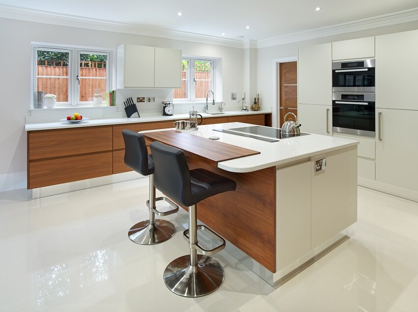 A bright kitchen with an island cream coloured countertops built in ceramic hob bar stools white tile floors and laminate cabinets
