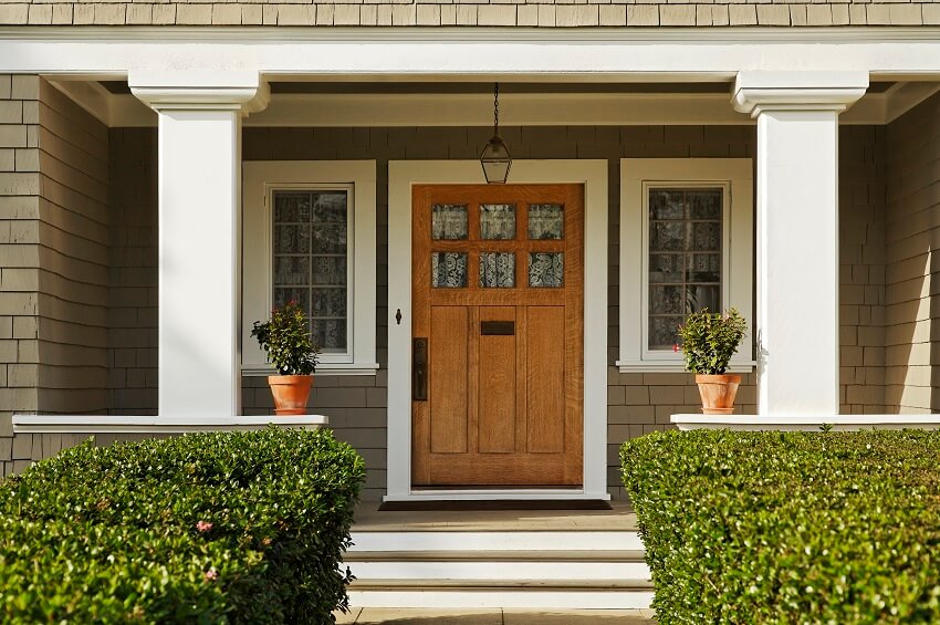 A concrete walkway with hedged shrubs leads to a solid wood front door with windows on both sides