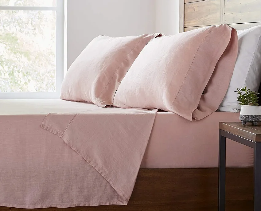 A queensize bed with pink stone & beam belgian flax linen bed sheet and plant on bedside table