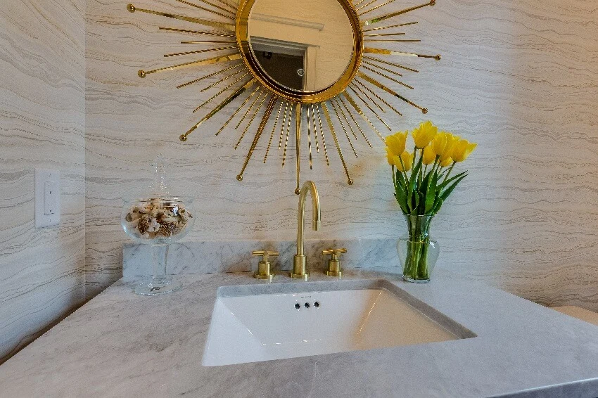 Bathroom sink with gold sun design mirror and faucet a glass vase with yellow tulips and stones