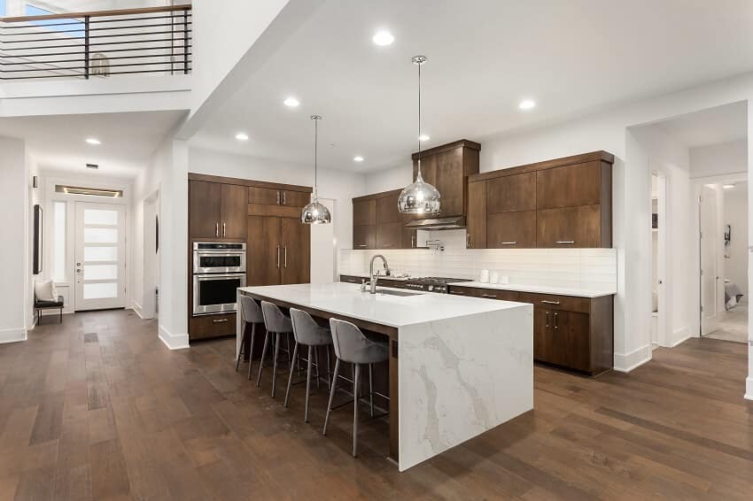 Beautiful kitchen with quartz waterfall island pendant lights, dark staggered cabinets, stainless steel appliances and hardwood floors