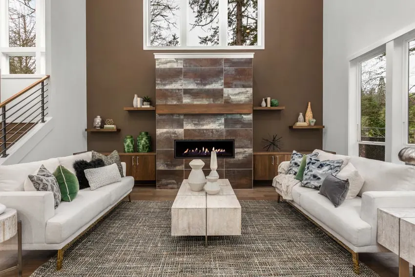 Beautiful living room with brown accent wall fireplace shelves white couches rug staircase glass windows