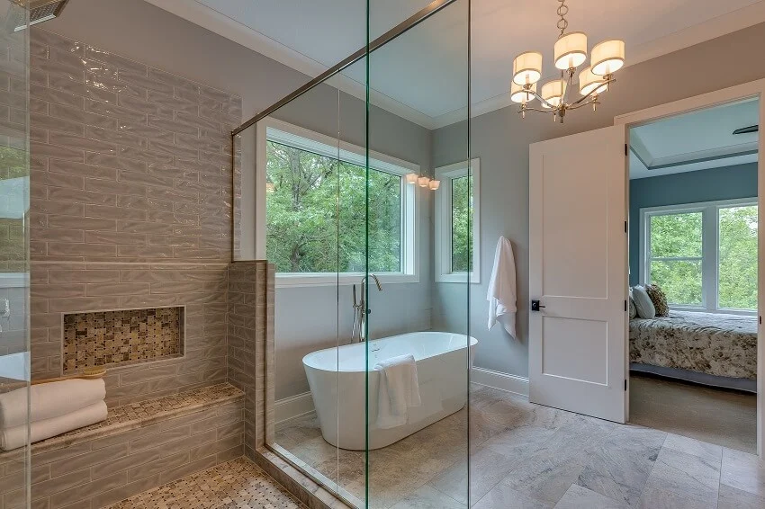 Bedroom connected to spacious bathroom with chandelier large glass shower and free standing bathtub