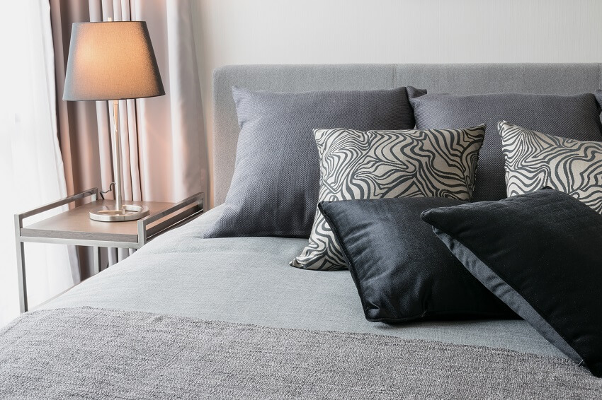 Bedroom interior design with black patterned pillows on bed and decorative table lamp