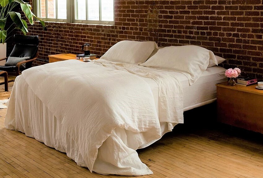 Bedroom with red brickwall wooden floor bedside table plants and queensize bed with huddleson ivory vintage washed pure italian linen sheet