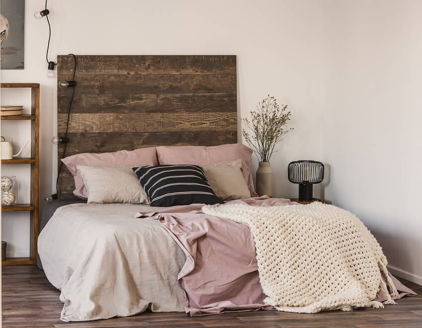 Bedroom with wood flooring string lights and bed with black and white pillow on pastel pink and beige linen sheets bedding