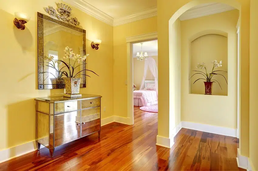 Bright hallway with wooden floor shiny cabinet mirror and arch niche in wall with decorative flowers