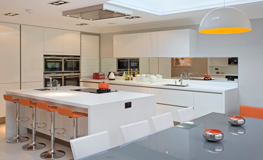 Bright kitchen with a large kitchen island with breakfast bar and orange bar stools and grey glass dining table