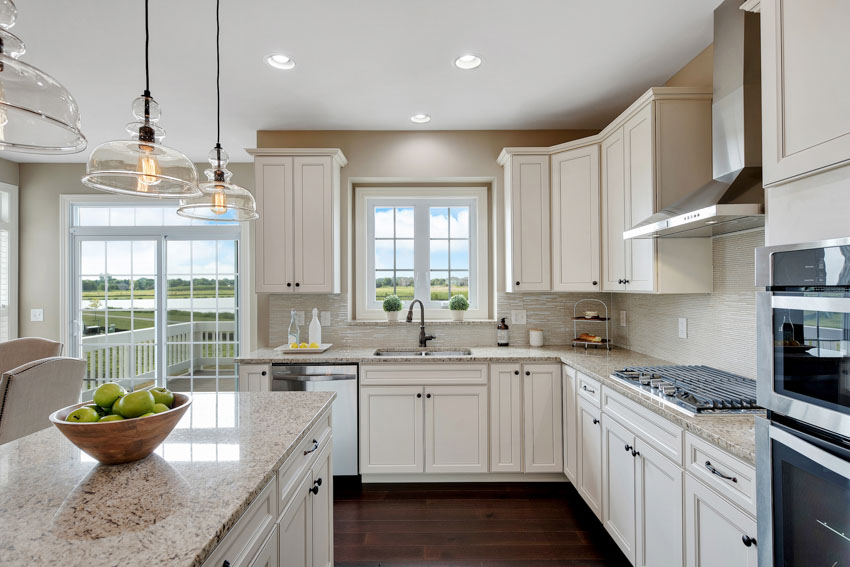 Classy kitchen with off white cabinets center island windows hanging lights stove oven hood wood floor