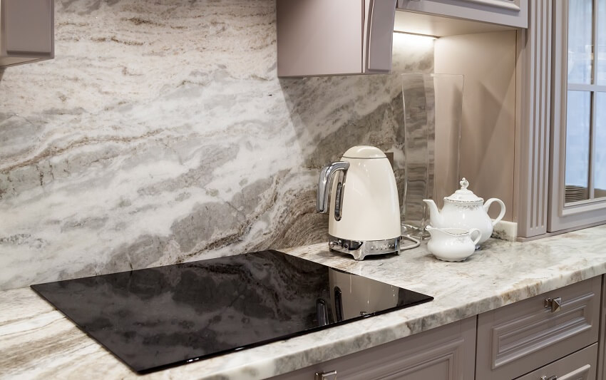 Closeup of custom designed kitchen with cream electric kettle with porcelain tea accessories on marble looking quartz countertop and backsplash