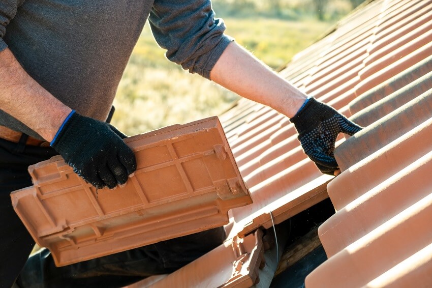 Closeup of worker hands installing yellow ceramic roofing tiles mounted on wooden boards