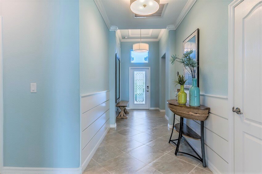 Console table with tile flooring and shiplap walls in a long corridor leading to front entrance