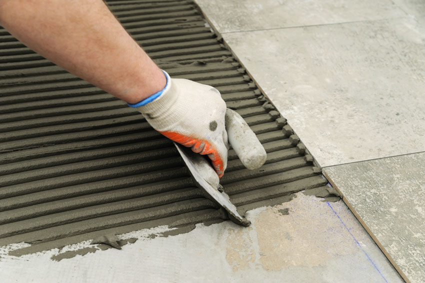 Contractor laying mortar on top of linoleum floor for tiles