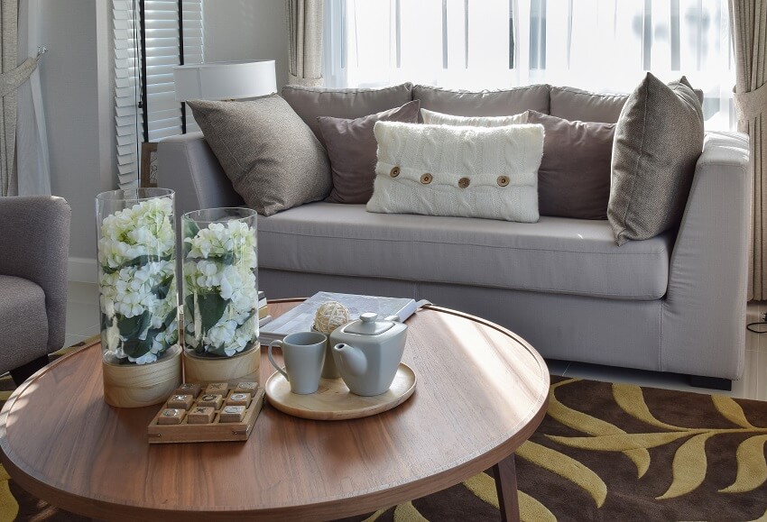 Decorative tea set and glass vase on wooden round table in living room interior