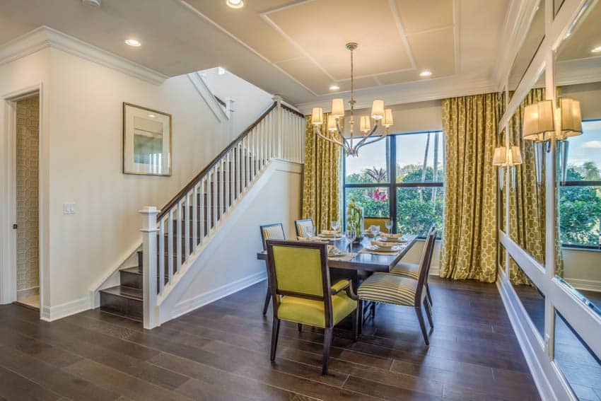 Dining space with wood floor hanging light staircase wall with artwork stair railing windows yellow curtain