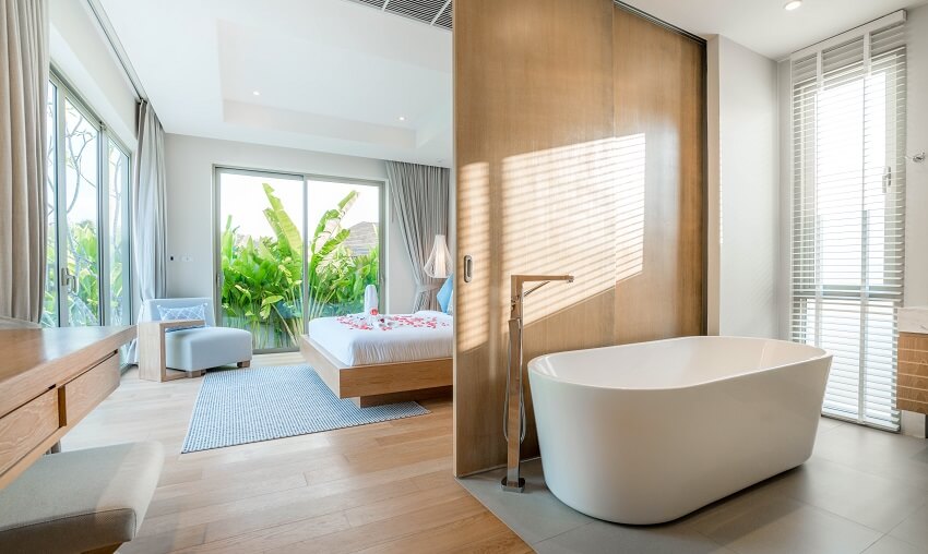 Ensuite bathroom and bedroom of pool villa with cozy bed bathtub brown and grey floor and a wooden sliding room divider