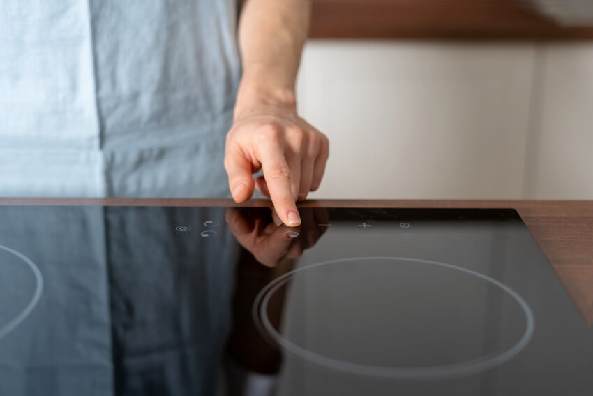 Finger on the power button at electric stove with glass ceramic surface