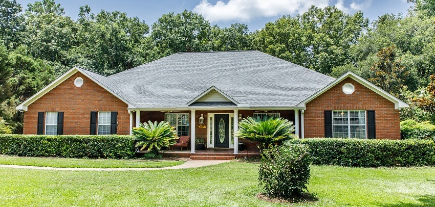 Front view of brown brick ranch house with a pathway and a spacious lawn and trees