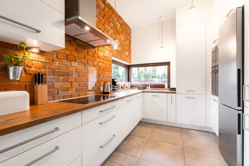 Galley kitchen farmhouse brick backsplash hood white cabinets drawers windows tile flooring