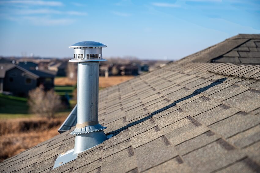 Galvanized metal chimney exhaust on asphalt roof with a rain cap