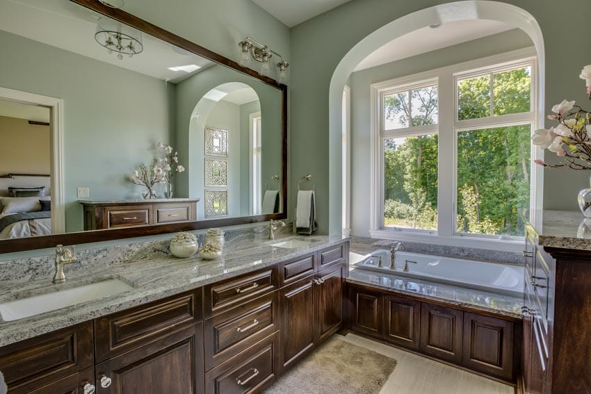Green wall bathroom wood accent cabinets drop in tub mirror countertop sink windows