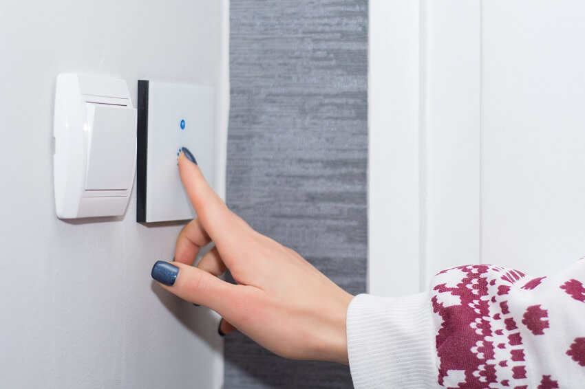Hand of a woman turning on or off a light on smart touch switch on a white wall