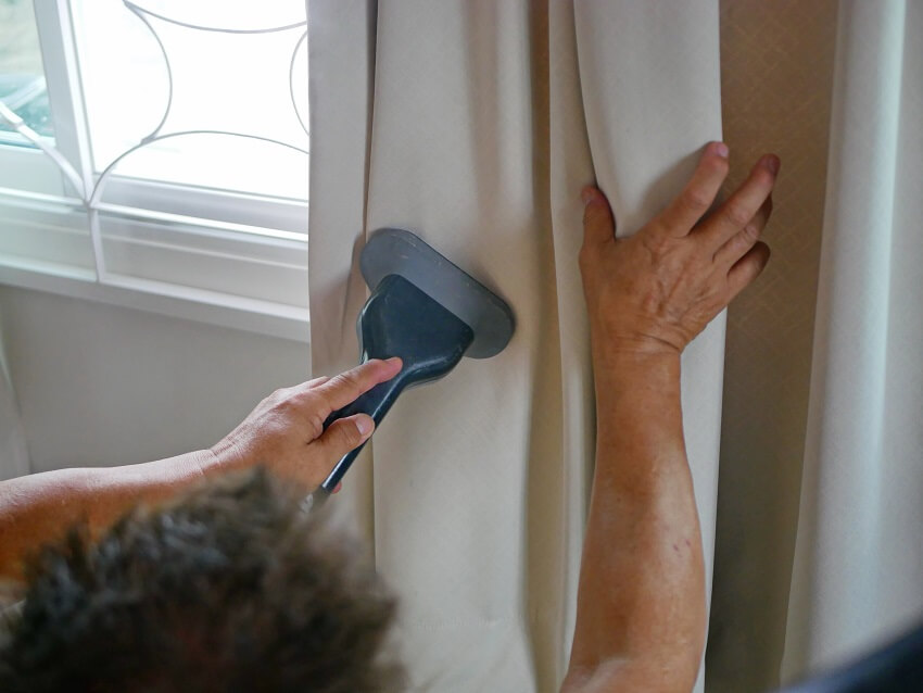 Hands of a man with a clothes or garment steamer to clean curtains