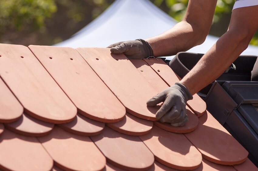 Hands of roofer laying natural red tile
