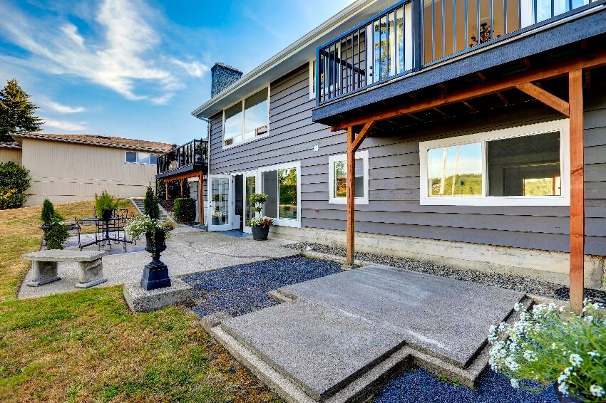 House with concrete foundation stone bench patio area and backyard walkout deck with black railings