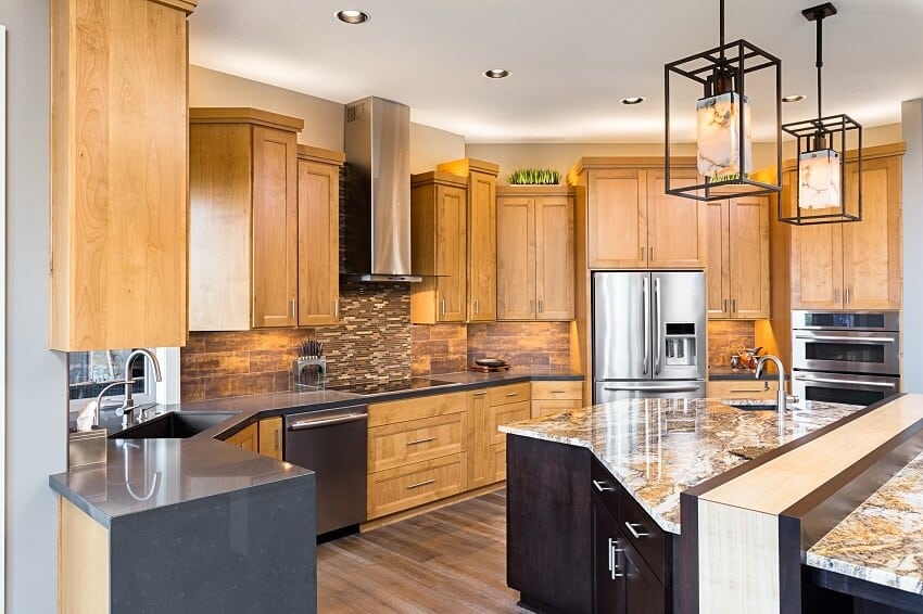 Kitchen in luxury home with island stainless steel appliances pendant lights and brown staggered cabinets