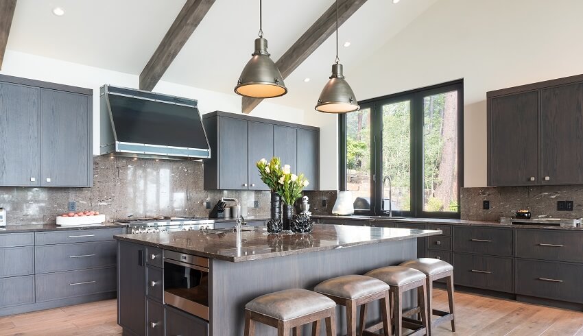 Kitchen island with stools and pendant lights above in a dark brown kitchen with beams on ceiling
