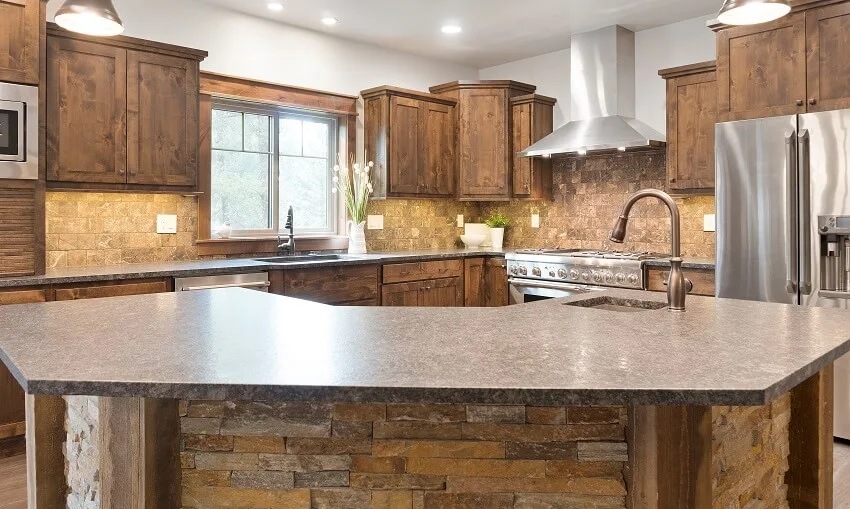 Kitchen with brown wood cabinets, stone backsplash and island with geometric shaped countertop