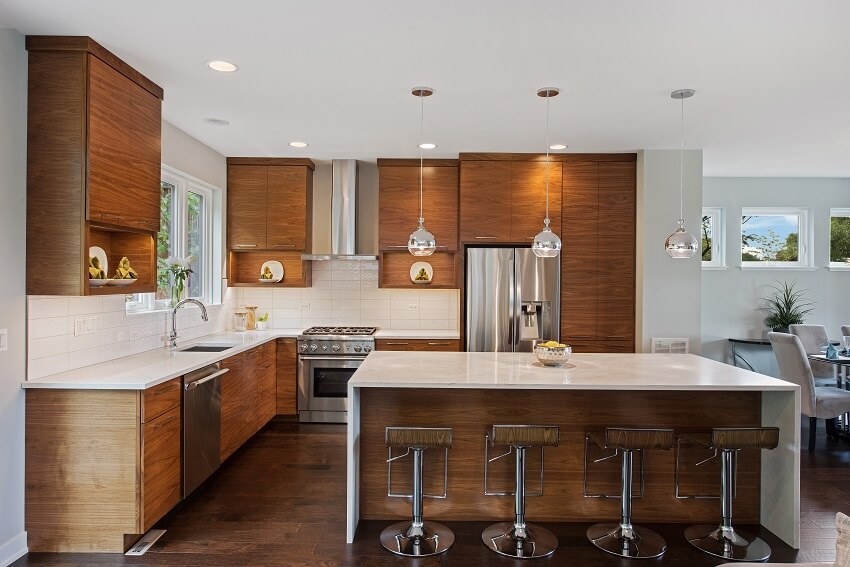 Kitchen with laminated brown cabinets hardwood floors and island with barstools white countertops pendant lights