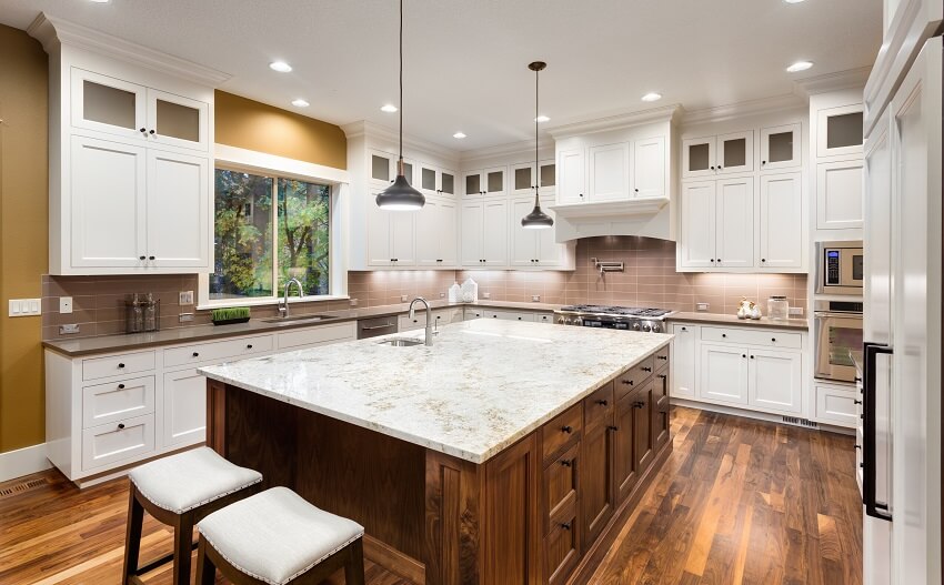 Kitchen with large island two sinks white cabinets pendant lights bar stools and hardwood floors