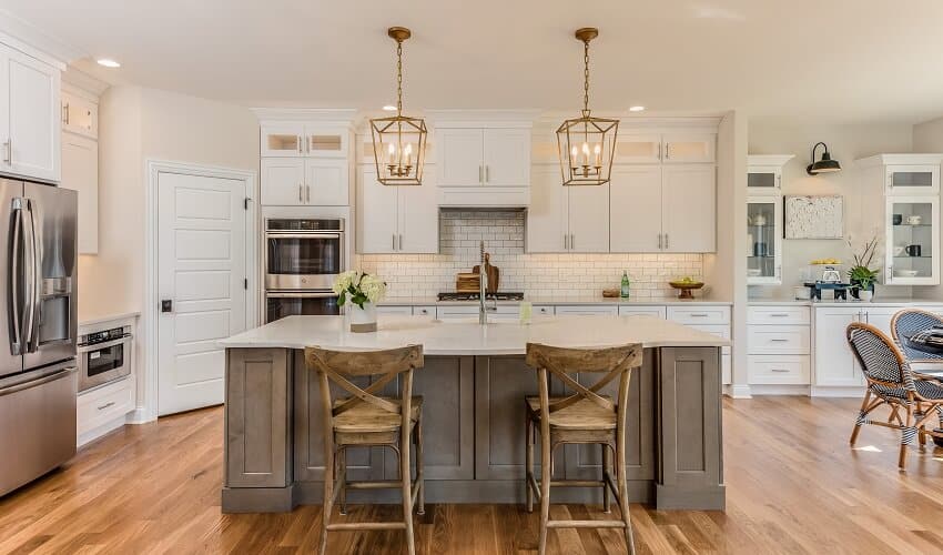 Kitchen with two pendant lights hang over kitchen island, staggered white cabinets and stainless steel appliances
