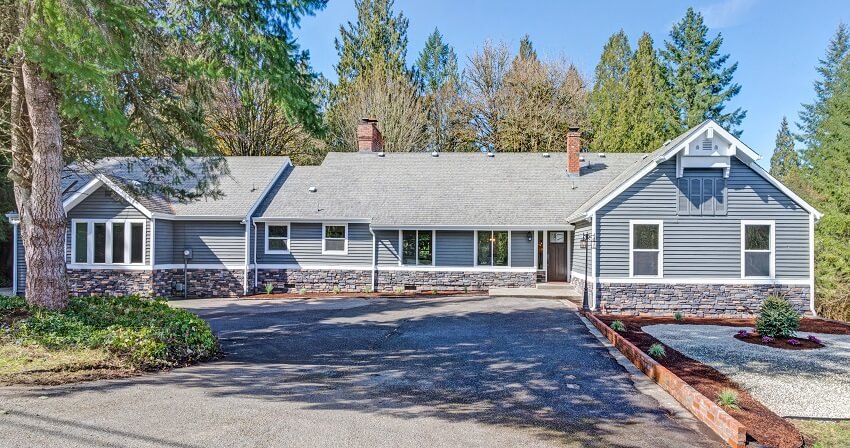 Large one story home with gray wood stone siding wide driveway and front yard