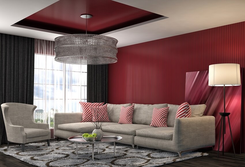 Living room with chandelier lamp shade carpet black curtain maroon wall and grey sofa with red striped cushion