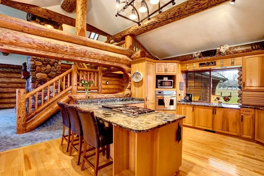 Log cabin kitchen interior with honey color cabinets island with stone countertop stainless steel appliance and view of staircase